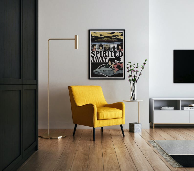 May include: A yellow armchair with black legs sits in a modern living room. A framed "Spirited Away" poster hangs on the wall. A gold floor lamp and a small side table with a vase of flowers complete the scene.
