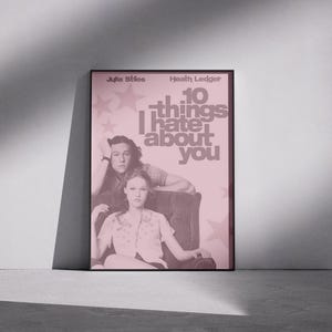 Pode incluir: Um cartaz de filme emoldurado para "10 Coisas que Eu Odeio em Você" com Julia Stiles e Heath Ledger. O cartaz tem um fundo rosa com estrelas e o título do filme em letras grandes e em negrito. Os atores estão no centro.