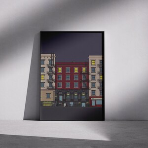 Könnte beinhalten: Ein gerahmter Kunstdruck mit einer stilisierten Illustration einer Stadtstraße bei Nacht. Das Kunstwerk zeigt mehrere Gebäude mit beleuchteten Fenstern in Beige-, Rot- und Gelbtönen. Der Druck wird vor einer weißen Wand präsentiert.