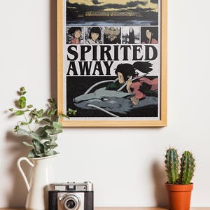 May include: A framed poster featuring the animated film "Spirited Away." The poster has a wooden frame and displays a scene with a girl riding a dragon-like creature. The title "Spirited Away" is prominently displayed.