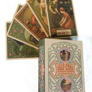 May include: A tarot card deck titled "Self-Care for Busy Women" with a matching box. The cards display vintage illustrations with floral borders and scenes of women. The box features the title in peach and green.