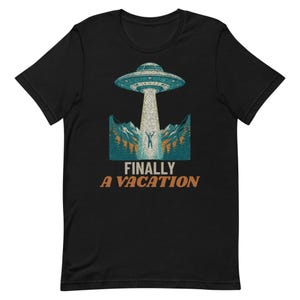 May include: A black t-shirt featuring a graphic of a flying saucer hovering over a mountain landscape with a person being beamed up. The text FINALLY A VACATION is printed in orange below the graphic. The design uses blue, white, and orange tones.