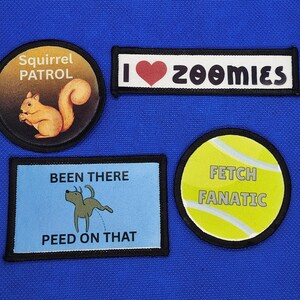 May include: Four embroidered patches with humorous designs. One patch features a squirrel with the text "Squirrel Patrol." Another says "I heart zoomies." A third patch shows a dog urinating with the text "Been There Peed on That." The last patch says "Fetch Fanatic."