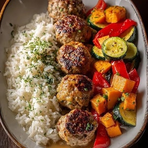 以下が含まれることがあります： ミートボール、白米、焼き野菜を盛り合わせた料理。ミートボールは焼き色がついており、ハーブを散らしたご飯の上にあります。焼き野菜には、赤ピーマン、ズッキーニ、バターナッツスクワッシュが含まれています。