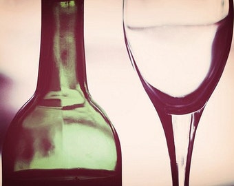 May include: A green glass wine bottle and a clear glass wine glass. The bottle is partially filled with red wine. The glass is empty.