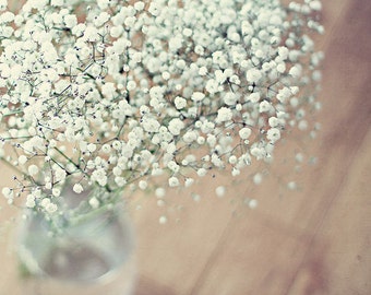 May include: A bouquet of white baby's breath flowers in a clear glass vase on a wooden surface.
