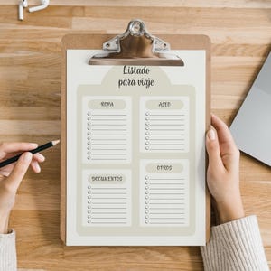 Puede incluir: Un portapapeles con una lista de verificación de viaje titulada "Listado para viaje". La lista se divide en cuatro secciones: "Ropa", "Aseo", "Documentos" y "Otros". Una mano sostiene un lápiz y un portátil es visible en el fondo.