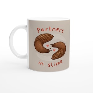May include: White ceramic mug with a whimsical design. The mug features two brown slugs with the text "partners in slime" in red. Two small red hearts are between the slugs. The mug has a white handle.