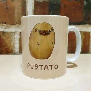 Może przedstawiać: Biały kubek ceramiczny z ilustracją brązowego ziemniaka w kształcie mopsa i napisem "pugtato" nadrukowanym z przodu.