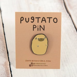 Könnte beinhalten: Eine braune Emaille-Anstecknadel in Form einer Kartoffel mit einem Mopsgesicht darauf. Die Anstecknadel trägt die Aufschrift "Pugtato Pin" und enthält die Website "sophiecorrigan.com" sowie Social-Media-Handles.