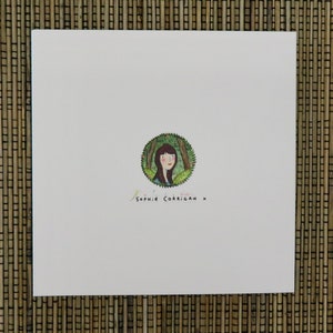 May include: A white card with a green circle containing a drawing of a woman with brown hair and a green dress. The text "Sophie Corrigan x" is written below the circle.