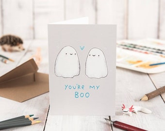 Op de afbeelding: Een kaart met twee cartoon-geesten en de tekst "You're my Boo". De kaart is lichtgrijs met een blauw hart tussen de geesten.