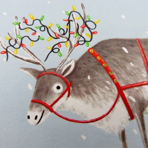 K&ouml;nnte beinhalten: Illustration eines Rentiers mit rotem Geschirr und einer Lichterkette mit bunten Weihnachtslichtern auf dem Geweih. Das Rentier ist grau mit wei&szlig;en Akzenten, vor einem hellblauen Hintergrund mit Schneeflocken.