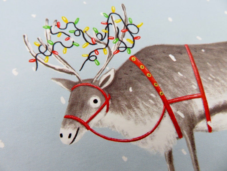 K&ouml;nnte beinhalten: Illustration eines Rentiers mit rotem Geschirr und einer Lichterkette mit bunten Weihnachtslichtern auf dem Geweih. Das Rentier ist grau mit wei&szlig;en Akzenten, vor einem hellblauen Hintergrund mit Schneeflocken.