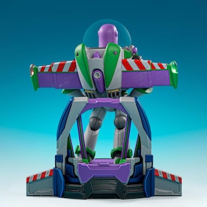 Könnte beinhalten: Eine Buzz Lightyear Actionfigur auf einem Präsentationssockel. Die Figur hat einen violetten Kopf, einen weiß-grünen Raumanzug mit Jetpack und ausgebreitete violette Flügel mit rot-weißen Streifen. Der Sockel ist in Blau und Violett gehalten.
