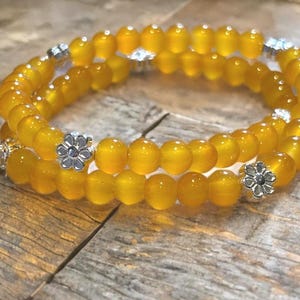 May include: A double-strand bracelet featuring translucent, round, golden-yellow beads. The bracelet is accented with small, silver-toned metal flower-shaped spacers placed at intervals along the strand, creating a consistent, repeating pattern.