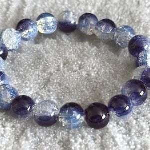 May include: A stretch bracelet composed of alternating round beads. The design features a mix of deep purple solid glass beads and light blue crackle glass beads that exhibit a translucent, icy appearance with internal fractures throughout.