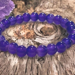 May include: A circular stretch bracelet composed of smooth, polished, deep purple spherical beads. The beads are uniform in size and arranged in a continuous loop, showcasing a consistent, vibrant violet hue throughout the entire piece.