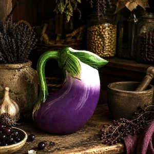 May include: A ceramic eggplant-shaped pitcher with a purple body, white top, and green handle and leaves. The pitcher is on a wooden surface with other kitchen items, including a mortar and pestle, garlic, and jars of spices.
