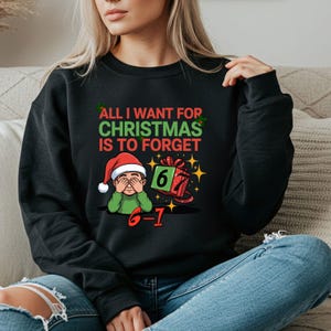 Może przedstawiać: Czarna bluza z napisem "ALL I WANT FOR CHRISTMAS IS TO FORGET". Grafika przedstawia postać z kreskówki w czapce Świętego Mikołaja, zasłaniającą oczy, oraz pudełko z prezentem z numerem 6-1.