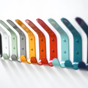 May include: A row of ten metal hooks in various colors, including black, white, green, gray, yellow, red, orange, light blue, dark blue, and navy blue. The hooks are all the same shape and size, and they are arranged in a line on a white background.