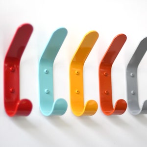May include: Five colorful metal hooks mounted on a white wall. The hooks are red, blue, yellow, orange, and gray.