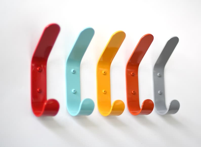 May include: Five colorful metal hooks mounted on a white wall. The hooks are red, blue, yellow, orange, and gray.