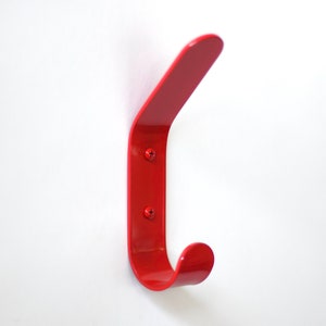 May include: A bright red metal hook mounted on a white wall. The hook is curved and has a rounded end.