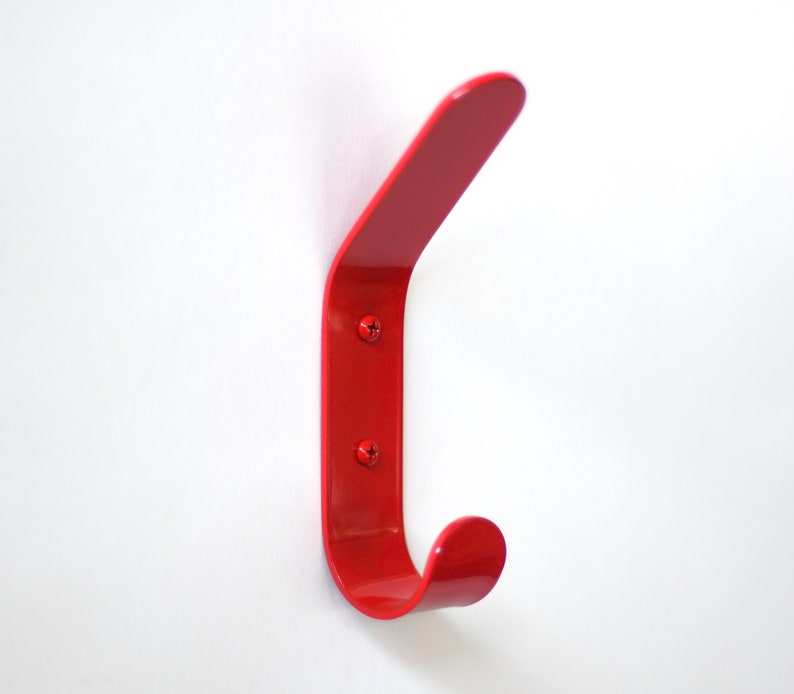 May include: A bright red metal hook mounted on a white wall. The hook is curved and has a rounded end.