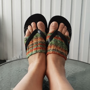 K&ouml;nnte beinhalten: Ein Paar schwarze Flip-Flops mit gr&uuml;nen, orangefarbenen und braunen Stricksocken. Die Socken werden &uuml;ber den F&uuml;&szlig;en getragen und reichen bis zu den Kn&ouml;cheln.
