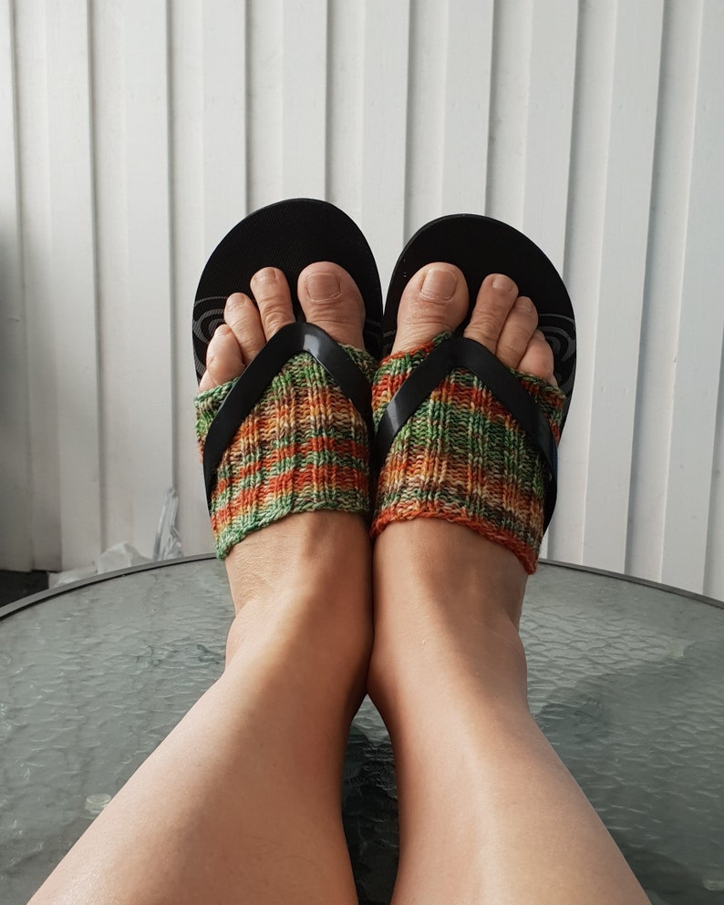 K&ouml;nnte beinhalten: Ein Paar schwarze Flip-Flops mit gr&uuml;nen, orangefarbenen und braunen Stricksocken. Die Socken werden &uuml;ber den F&uuml;&szlig;en getragen und reichen bis zu den Kn&ouml;cheln.