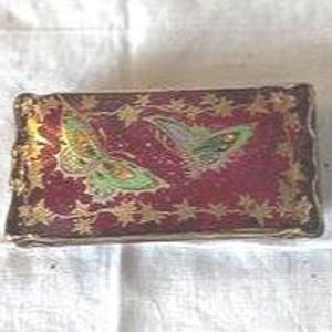May include: A rectangular trinket box with a burgundy background and gold trim. Two green and yellow butterflies are painted on the lid. The box is resting on a white, textured surface.