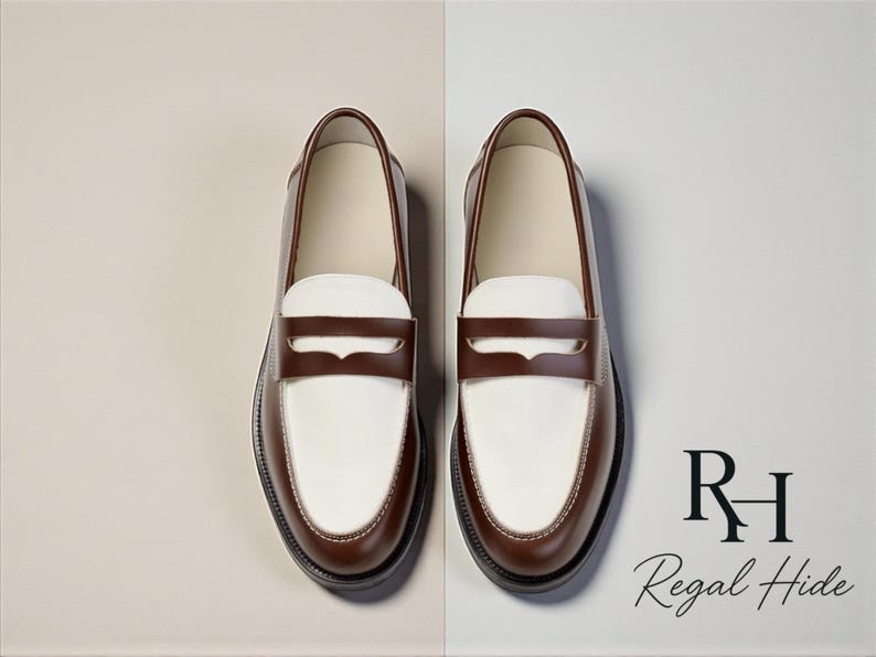 May include: A pair of two-tone leather loafers. The shoes have a white vamp and a brown saddle strap and trim. The soles are black. The brand name "Regal Hide" is displayed in the lower right corner.