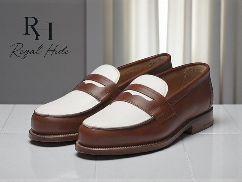 May include: A pair of brown and white leather penny loafers. The shoes have a classic design with a brown leather upper, white vamp, and a penny strap. The shoes are displayed on a white surface.