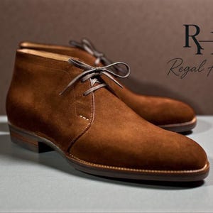 May include: A pair of brown suede chukka boots with matching laces. The boots have a classic design with a rounded toe and a low heel. The brand name "Regal Hide" is displayed in the upper right corner.