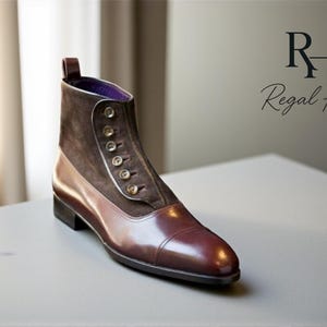 Puede incluir: Botín de cuero marrón y burdeos con empeine de ante y cierre de botones. La bota tiene un acabado pulido y un tacón pequeño. El logotipo de Regal Hide está en el fondo.