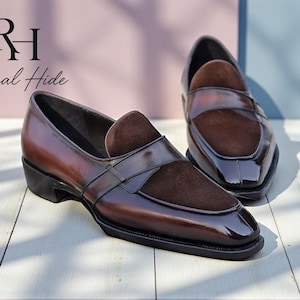 May include: A pair of brown leather loafers with a suede vamp and a glossy finish. The shoes have a square toe and a strap detail across the top. The Regal Hide logo is in the upper left corner.
