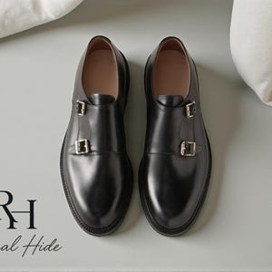 May include: A pair of black leather double monk strap shoes with silver buckles. The shoes have a polished finish and are displayed on a light gray surface. The brand name "Regal Hide" is visible in the lower left corner.