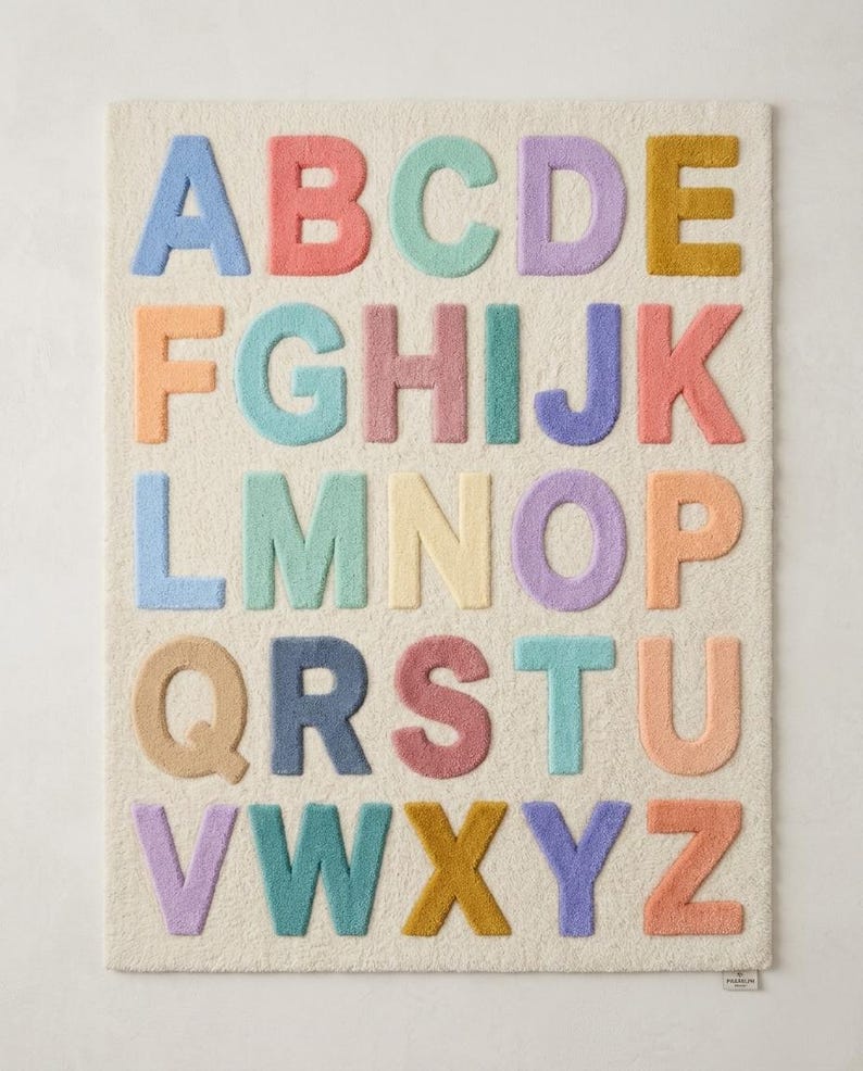 May include: A rectangular off-white rug featuring the English alphabet in raised, tufted letters. Each letter is rendered in a distinct pastel color, including shades of blue, pink, teal, purple, yellow, and orange, arranged in five rows of five letters.