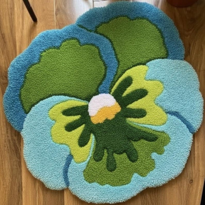 May include: A colorful, flower-shaped rug with a tufted texture. The rug features a vibrant palette of blue, green, and yellow, with a white and yellow center. The design resembles a large pansy, adding a touch of nature-inspired decor.