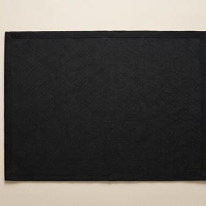 May include: A rectangular black placemat featuring a solid dark color and a clean, finished border edge. The surface has a subtle, fine-grained texture throughout, providing a consistent and uniform appearance across the entire flat rectangular shape.