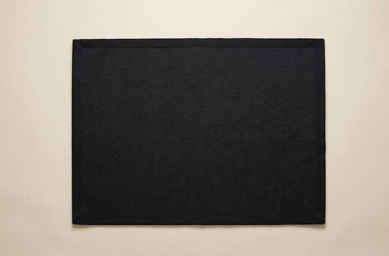 May include: A rectangular black placemat featuring a solid dark color and a clean, finished border edge. The surface has a subtle, fine-grained texture throughout, providing a consistent and uniform appearance across the entire flat rectangular shape.