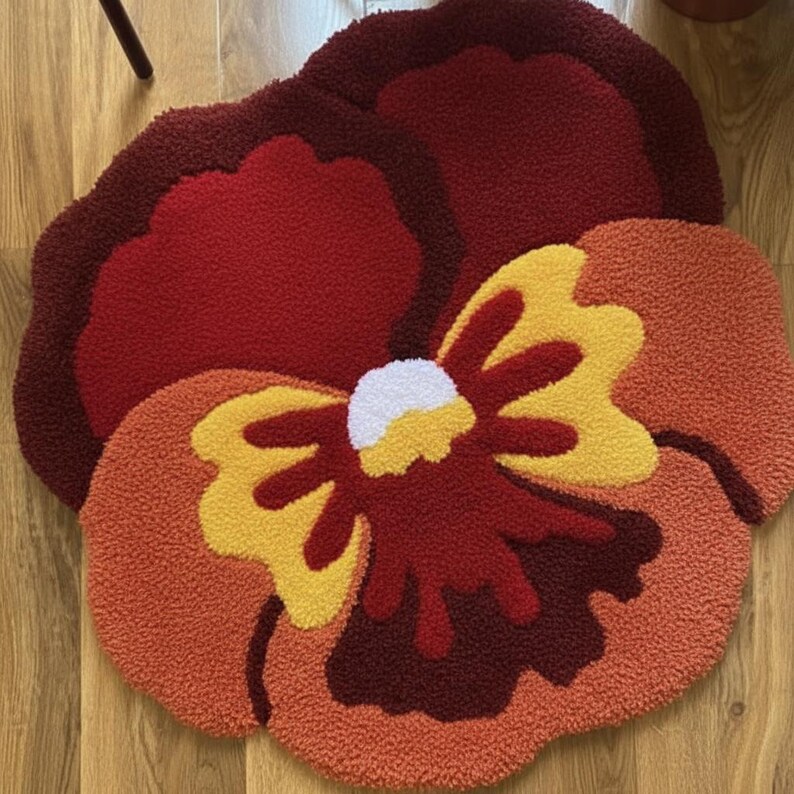 May include: A flower-shaped rug with a vibrant design. The rug features a large, multi-layered flower in shades of red, orange, and yellow. The center of the flower is white. The rug is made of a soft, textured material.