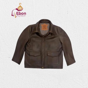 Könnte beinhalten: Braune Lederjacke mit zwei Vordertaschen und einem Kragen. Die Jacke hat einen Knopfverschluss und ein kleines Etikett innen mit der Aufschrift "GENUINE 100% LEATHER". Die Jacke ist ein klassischer Stil.