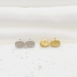May include: Two pairs of pumpkin-shaped stud earrings. One pair is finished in a polished silver tone, while the other pair is finished in a polished gold tone. Each earring features vertical ridges and a small stem at the top of the pumpkin shape.