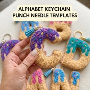 Könnte beinhalten: Alphabet-Schlüsselanhänger-Punch-Needle-Vorlagen. Das Bild zeigt mehrere handgefertigte Schlüsselanhänger in Form von Buchstaben. Die Buchstaben sind beige mit farbenfrohem Zuckerguss und Streuseln, und jeder hat eine Quaste und einen Schlüsselring.