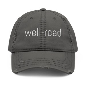 May include: A grey, distressed baseball cap with the white embroidered text "well-read". The cap features a curved peak and a worn, vintage appearance, with distressed detailing around the edges.