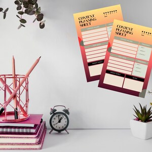 Op de afbeelding: Een bureauscène met roze notitieboekjes, potloden en een geometrische pennenhouder. Twee "Content Planning Sheet" prints met een verloopachtergrond worden weergegeven. Een kleine wekker en potplanten maken de scène compleet.