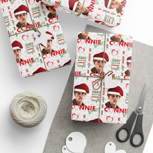 Peut inclure: Des cadeaux emballés avec du papier cadeau festif représentant un homme avec un bonnet de Père Noël, des cœurs et du texte. Les cadeaux sont attachés avec de la ficelle et ont des étiquettes vierges.