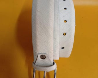 Puede incluir: Un cinturón de cuero blanco con hebilla plateada. El cinturón tiene una superficie texturizada y varios agujeros para ajustar. La hebilla es rectangular y tiene un acabado plateado. El cinturón está enrollado, mostrando toda su longitud.